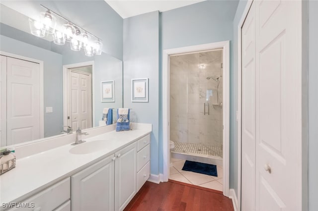 full bathroom with toilet, wood finished floors, vanity, a closet, and a stall shower