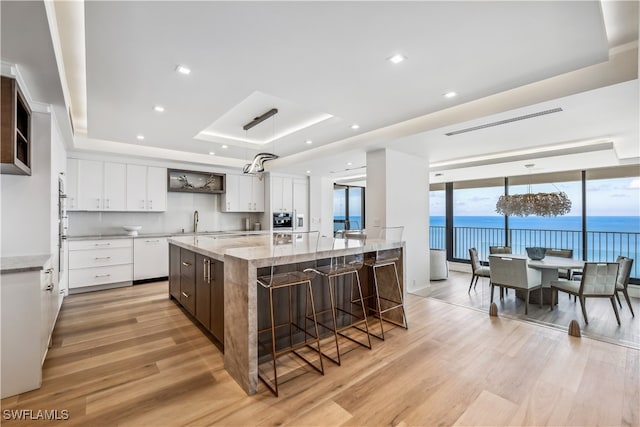 kitchen featuring white cabinetry, a large island, a raised ceiling, light hardwood / wood-style floors, and a water view