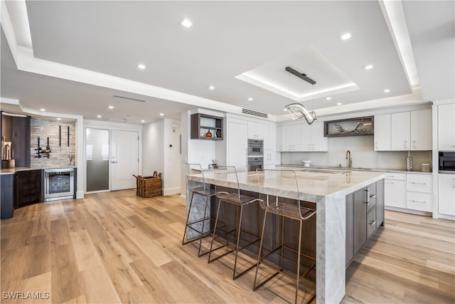 kitchen with a raised ceiling, light hardwood / wood-style flooring, white cabinets, and a breakfast bar area