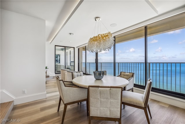 dining room featuring a healthy amount of sunlight, a water view, light hardwood / wood-style floors, and an inviting chandelier