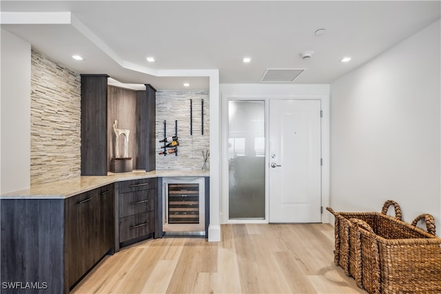 bar featuring dark brown cabinets, light stone counters, wine cooler, and light hardwood / wood-style flooring