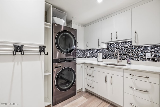 laundry room with cabinets, stacked washer and dryer, light hardwood / wood-style flooring, and sink