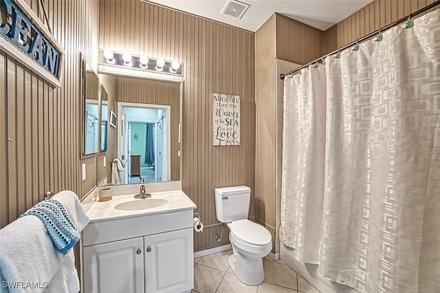 bathroom with a textured ceiling, vanity, wooden walls, tile patterned flooring, and toilet