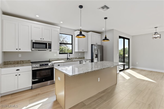 kitchen with light stone countertops, stainless steel appliances, a kitchen island, decorative light fixtures, and white cabinets