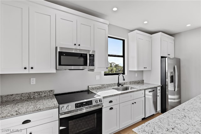 kitchen with light stone countertops, white cabinetry, sink, stainless steel appliances, and light hardwood / wood-style floors