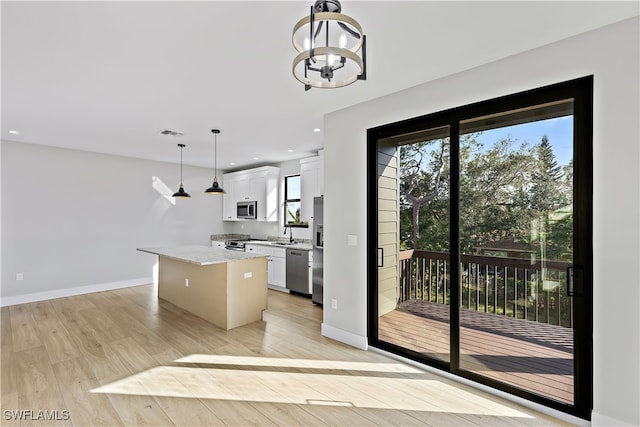 kitchen featuring appliances with stainless steel finishes, decorative light fixtures, a kitchen island, light stone counters, and white cabinetry