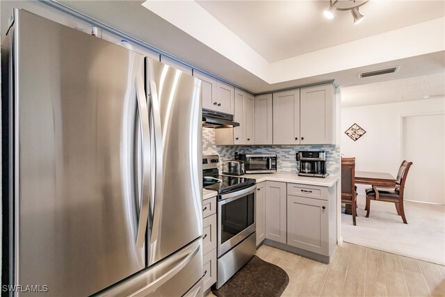 kitchen with light hardwood / wood-style flooring, stainless steel appliances, a tray ceiling, backsplash, and gray cabinets