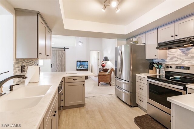 kitchen featuring decorative light fixtures, a barn door, sink, a raised ceiling, and appliances with stainless steel finishes