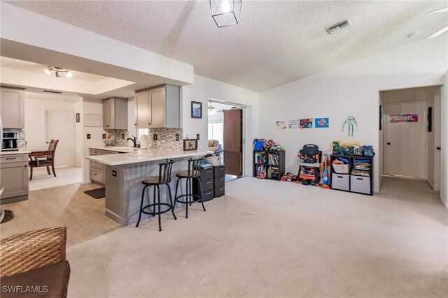 kitchen with tasteful backsplash, gray cabinetry, a breakfast bar area, a raised ceiling, and kitchen peninsula