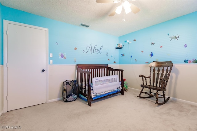 bedroom with a crib, carpet, ceiling fan, and a textured ceiling