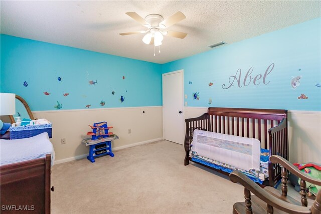 bedroom with light carpet, ceiling fan, a crib, and a textured ceiling