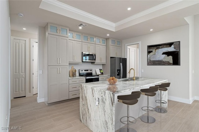 kitchen with light wood finished floors, visible vents, stainless steel appliances, a raised ceiling, and a sink