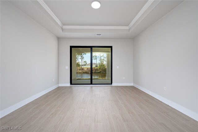 empty room with light wood-type flooring, a raised ceiling, and crown molding