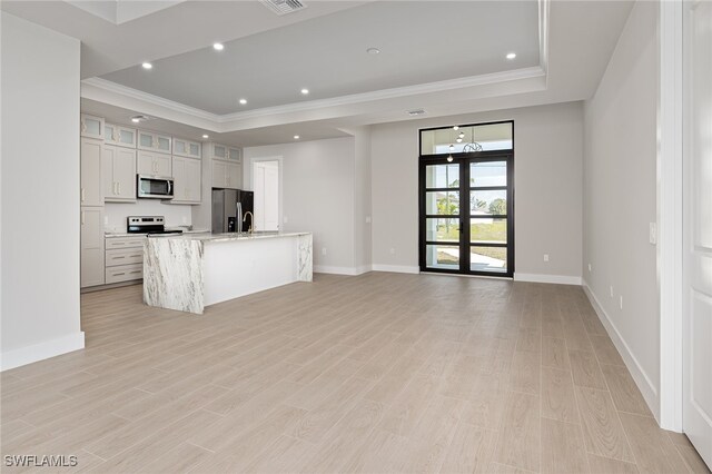 kitchen featuring light stone counters, stainless steel appliances, light hardwood / wood-style floors, a tray ceiling, and an island with sink