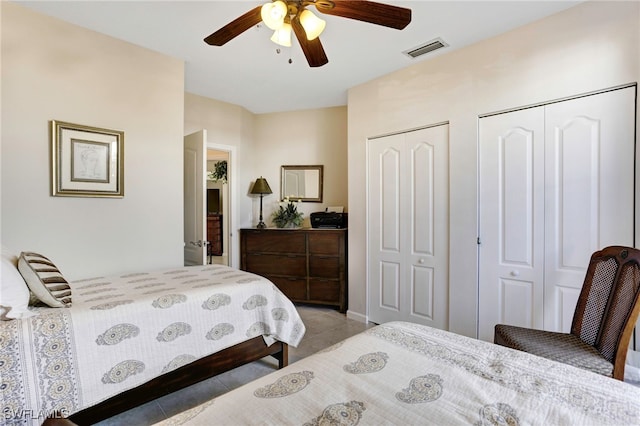 bedroom featuring light tile patterned floors, visible vents, multiple closets, and a ceiling fan