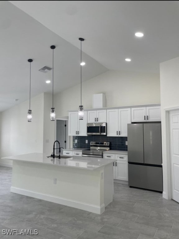 kitchen with an island with sink, vaulted ceiling, stainless steel appliances, and white cabinetry