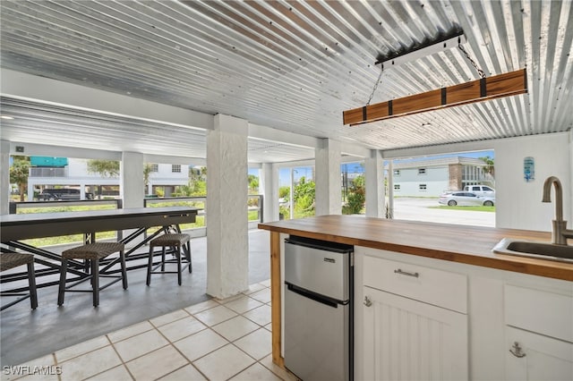 kitchen with light tile patterned floors, wooden counters, freestanding refrigerator, white cabinets, and a sink