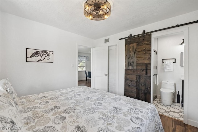 bedroom with a barn door, a textured ceiling, visible vents, and dark wood-style flooring