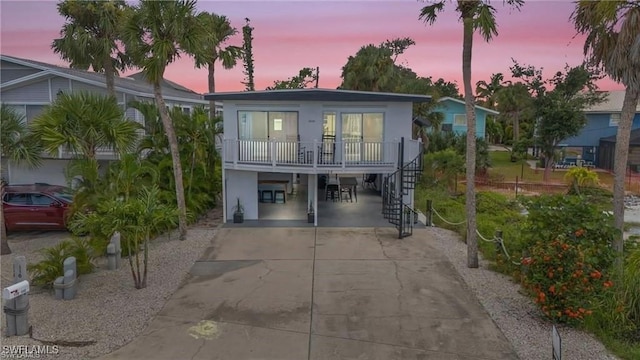 view of front facade featuring covered porch, stairs, driveway, stucco siding, and a carport