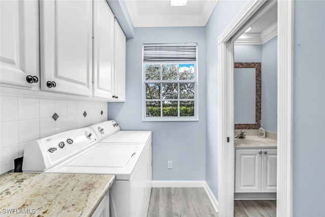 clothes washing area featuring light wood-style flooring, baseboards, washer and dryer, ornamental molding, and cabinet space