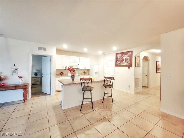 kitchen featuring a breakfast bar area, white appliances, light tile patterned floors, a center island, and white cabinets