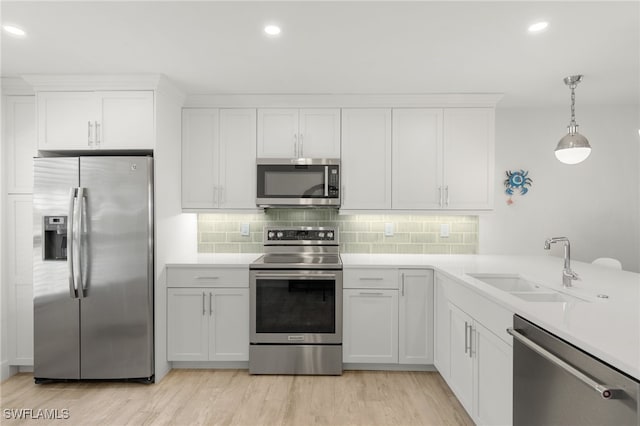 kitchen featuring appliances with stainless steel finishes, white cabinets, decorative light fixtures, and light wood-type flooring