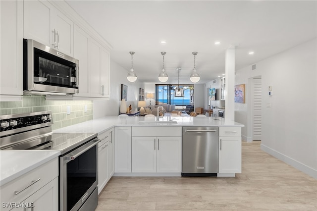 kitchen featuring hanging light fixtures, kitchen peninsula, stainless steel appliances, white cabinetry, and light hardwood / wood-style floors