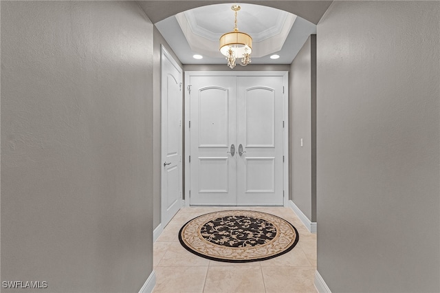 doorway with crown molding, a raised ceiling, a notable chandelier, and light tile patterned flooring