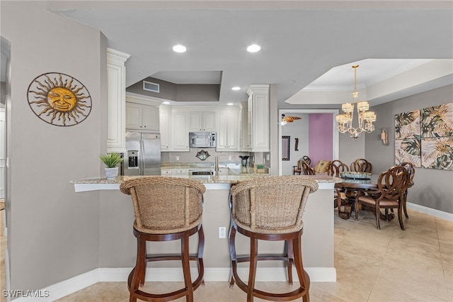 kitchen with light stone countertops, stainless steel appliances, a chandelier, a raised ceiling, and a breakfast bar area