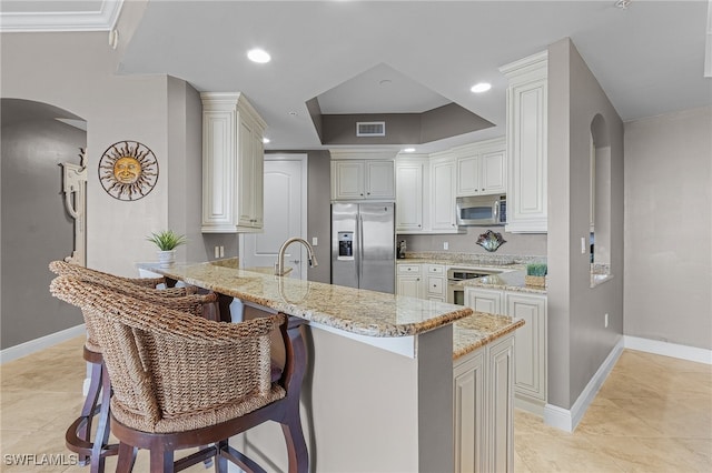 kitchen with stainless steel appliances, a kitchen breakfast bar, kitchen peninsula, sink, and light stone countertops