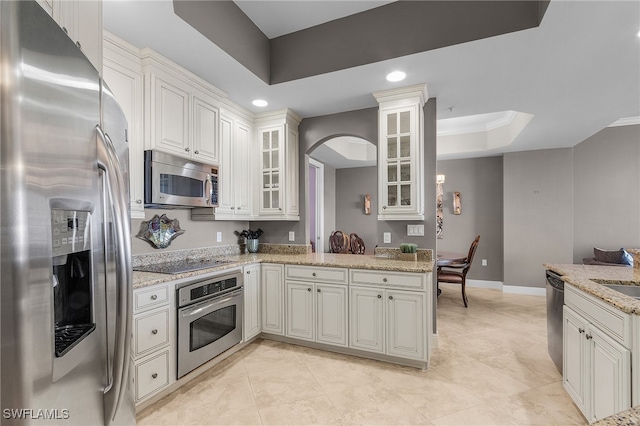 kitchen featuring appliances with stainless steel finishes, light stone counters, a raised ceiling, and white cabinetry