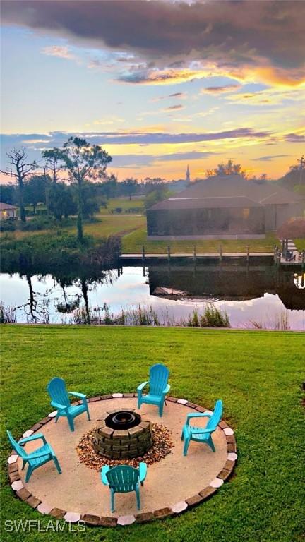 playground at dusk featuring a water view, a lawn, and a fire pit