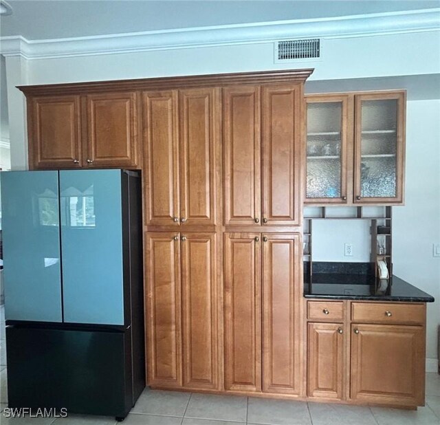 kitchen featuring visible vents, ornamental molding, freestanding refrigerator, dark stone counters, and glass insert cabinets