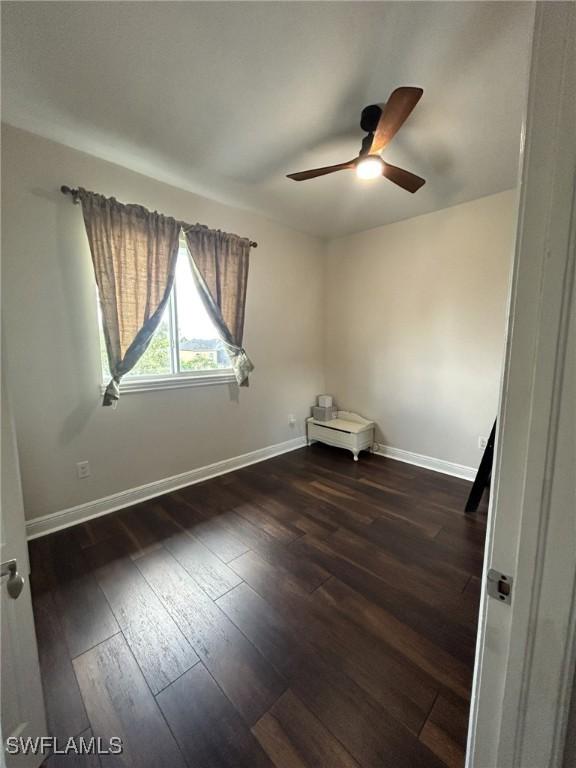 empty room with ceiling fan, dark wood finished floors, and baseboards