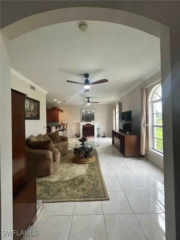 living area featuring light tile patterned floors, a ceiling fan, arched walkways, and crown molding