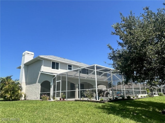 back of house featuring a yard, a chimney, a lanai, and stucco siding