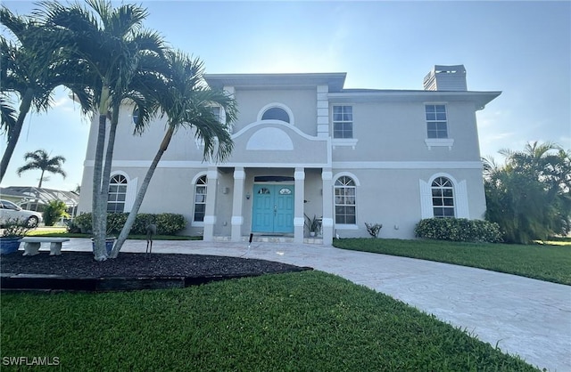 view of front of house with a front yard, a chimney, and stucco siding