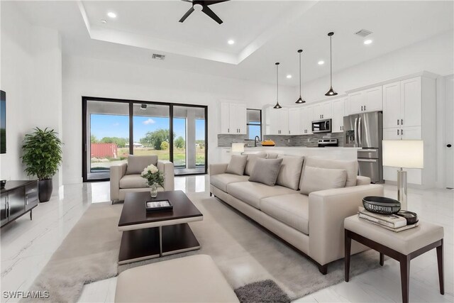 living room featuring a raised ceiling, ceiling fan, sink, and a high ceiling