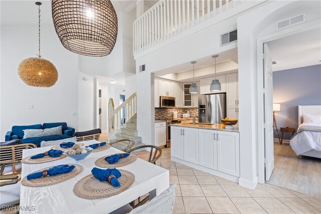 kitchen with pendant lighting, stainless steel appliances, white cabinetry, and a high ceiling