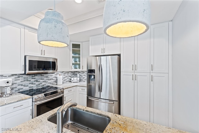 kitchen featuring appliances with stainless steel finishes, white cabinetry, light stone countertops, pendant lighting, and sink