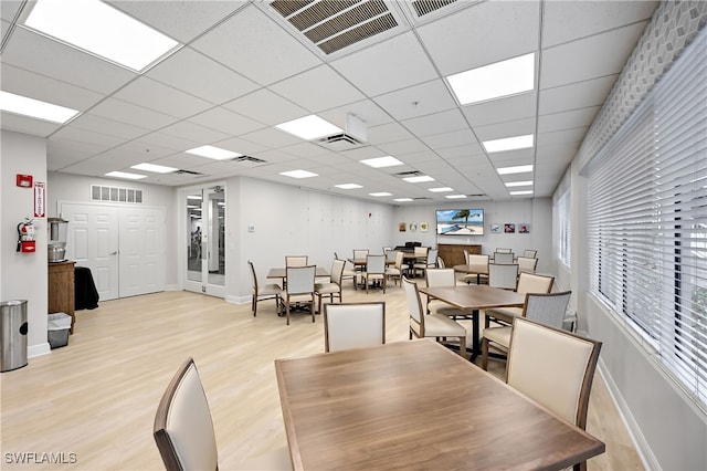 dining space with light wood-type flooring, a drop ceiling, and french doors