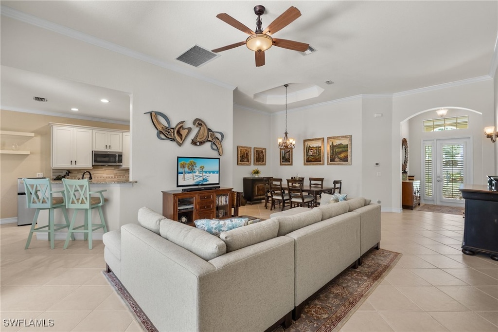 living room with ceiling fan with notable chandelier, light tile patterned floors, ornamental molding, and french doors