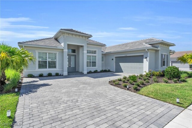 prairie-style house with stucco siding, a tile roof, decorative driveway, and a garage