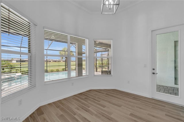 spare room featuring light wood finished floors, a notable chandelier, crown molding, and baseboards