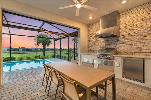 patio terrace at dusk with an outdoor pool, an outdoor kitchen, a grill, and glass enclosure