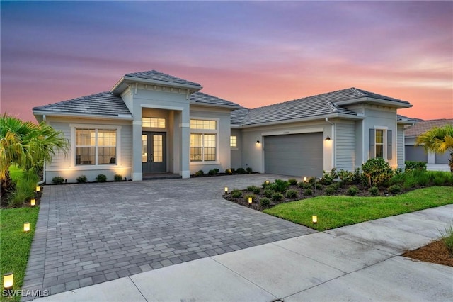 view of front facade with stucco siding, a tile roof, decorative driveway, french doors, and an attached garage