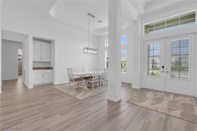 unfurnished dining area with a towering ceiling, french doors, plenty of natural light, and light hardwood / wood-style flooring