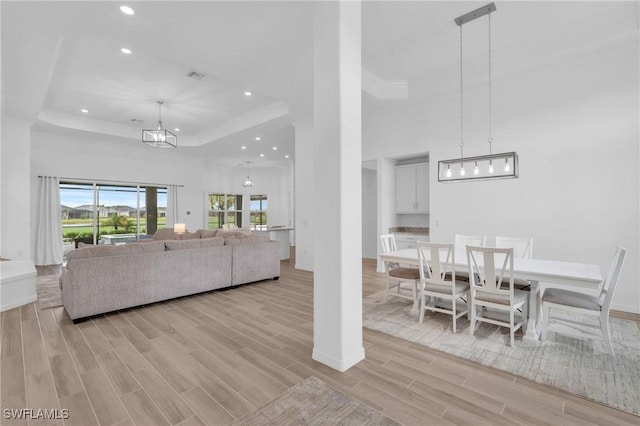 living area with wood finish floors, a tray ceiling, recessed lighting, a high ceiling, and an inviting chandelier