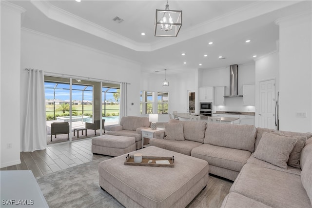 living room featuring ornamental molding, light hardwood / wood-style flooring, an inviting chandelier, sink, and a tray ceiling