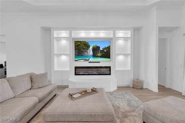 living area featuring a glass covered fireplace, crown molding, built in shelves, and wood finished floors